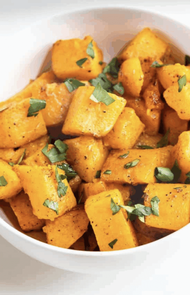 A white bowl filled with roasted butternut squash cubes, seasoned with black pepper and garnished with chopped fresh parsley.