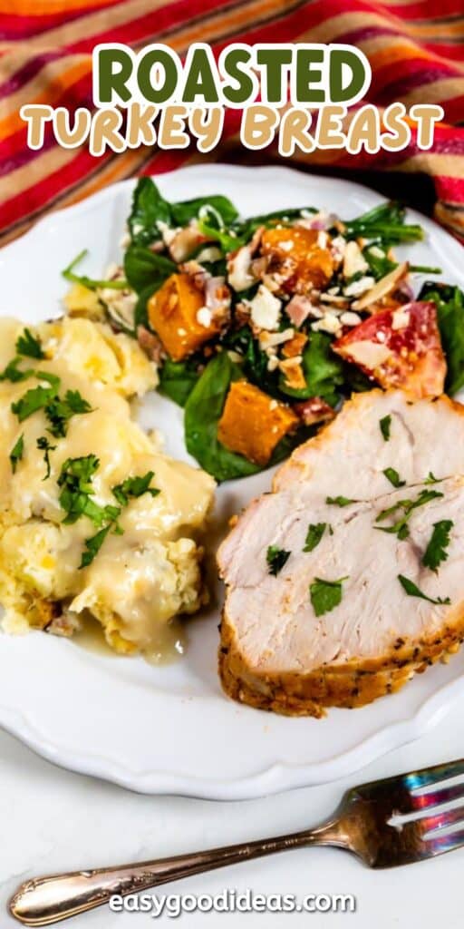 A dinner plate with sliced roasted turkey breast, mashed potatoes topped with gravy, and a spinach salad with roasted sweet potatoes and feta cheese. A fork is beside the plate on a white table.