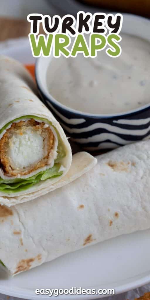 Close-up of two turkey wraps filled with lettuce, one cut open to show the filling, served on a white plate next to a bowl of creamy dipping sauce. Text reads Turkey Wraps and easygoodideas.com.