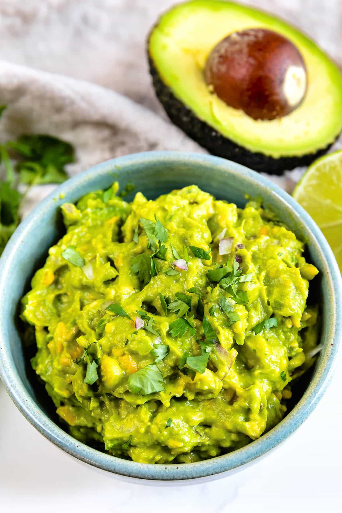 A bowl of fresh guacamole topped with chopped cilantro, with a halved avocado and lime wedge in the background.