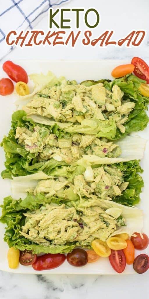 A white platter with three lettuce leaves filled with creamy keto chicken salad, surrounded by assorted halved cherry tomatoes. The text above reads KETO CHICKEN SALAD.