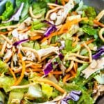 A bowl of Asian-inspired salad with chopped romaine lettuce, shredded carrots, purple cabbage, sliced almonds, shredded chicken, and crispy noodles.